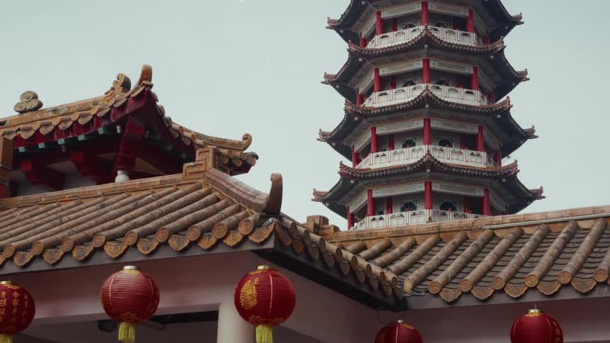 A traditional Chinese pagoda towers over tiled temple roofs decorated with red paper lanterns on a calm, overcast day