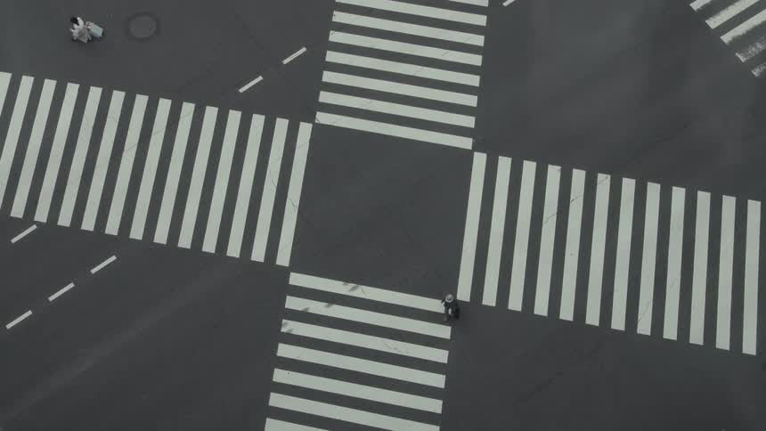 An abstract, top-down perspective of a quiet city intersection as a few people cross the street