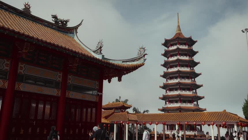A wide shot captures the stunning architecture of a traditional Chinese temple and pagoda as visitors explore the grounds under a cloudy sky