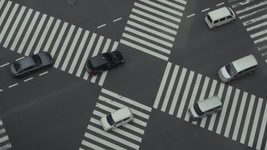 A high-angle, overhead view shows the intricate and hypnotic flow of traffic, including cars, buses, and trucks, through a busy urban intersection