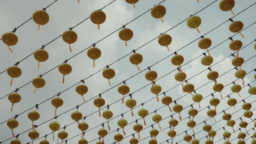 A low-angle view shows rows of yellow Chinese lanterns swaying gently against an overcast sky