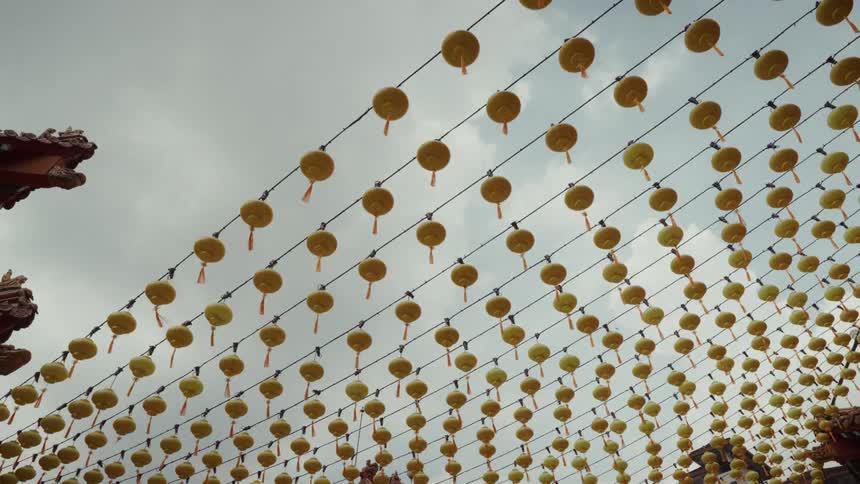 A low-angle view shows countless yellow Chinese lanterns hanging in neat rows against a cloudy sky at a temple