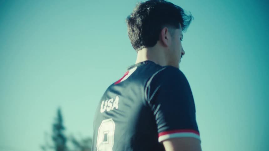 Cinematic slow motion shot of a determined young man in a USA soccer jersey standing against a clear blue sky