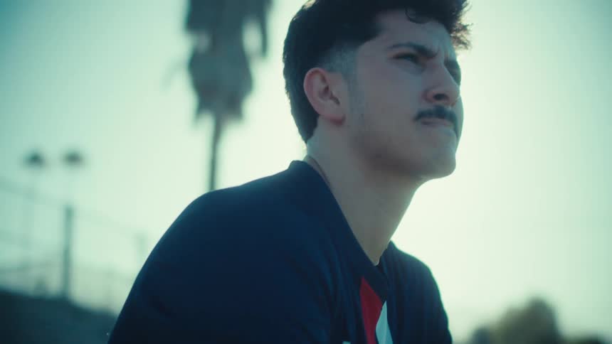 A determined young soccer player in a USA jersey sits with his ball on the sidelines, mentally preparing for the game under the bright sun