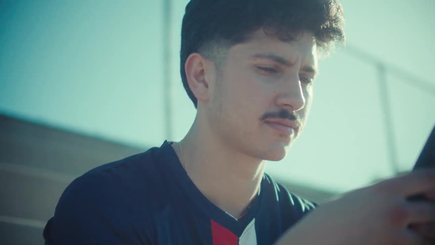 Close up of a young athlete sitting on stadium steps looking at his phone on a sunny day