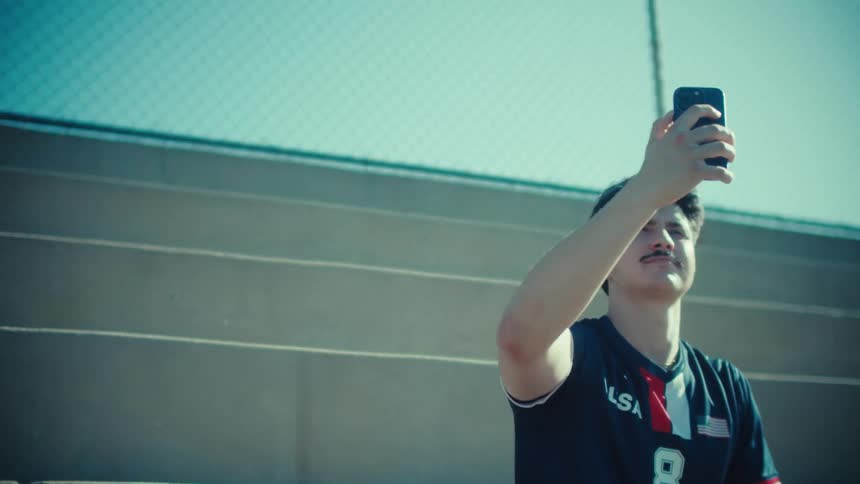 A proud young athlete in a USA soccer jersey takes a selfie while sitting on stadium bleachers