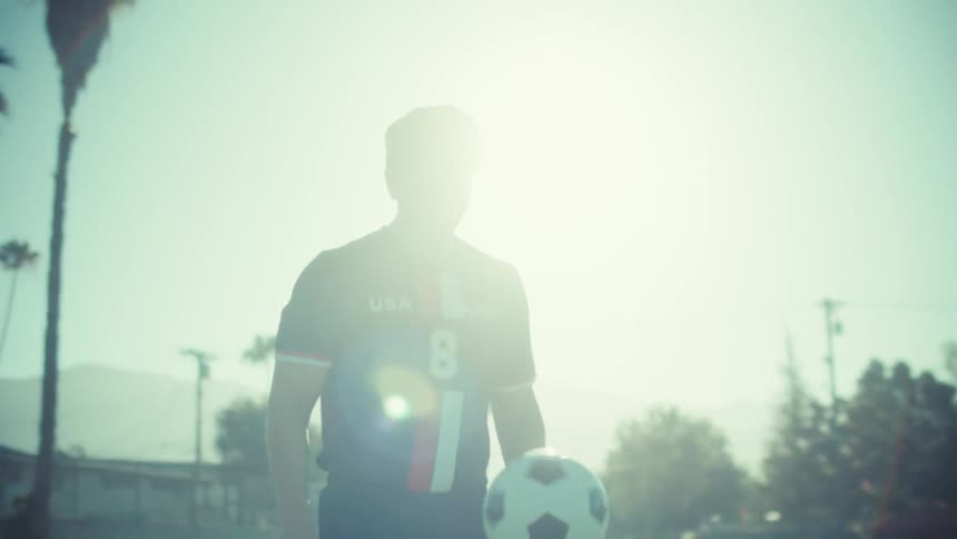 In slow motion, a focused soccer player in a USA jersey practices his ball-handling skills on a sunny field