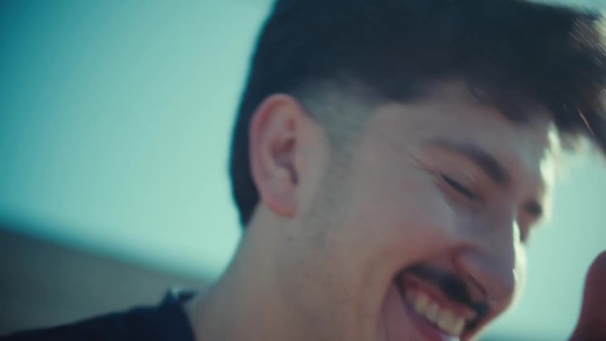 Close up of a joyful young man laughing hysterically while scrolling through his smartphone on a bright sunny day