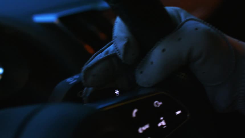 A close-up shot of a gloved hand on the steering wheel of a modern car at night