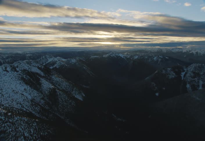 The sun rises over a vast, shadowy mountain range partially covered in snow