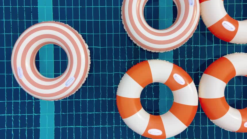 Colorful striped inflatable rings gently float in a clear blue swimming pool on a summer day