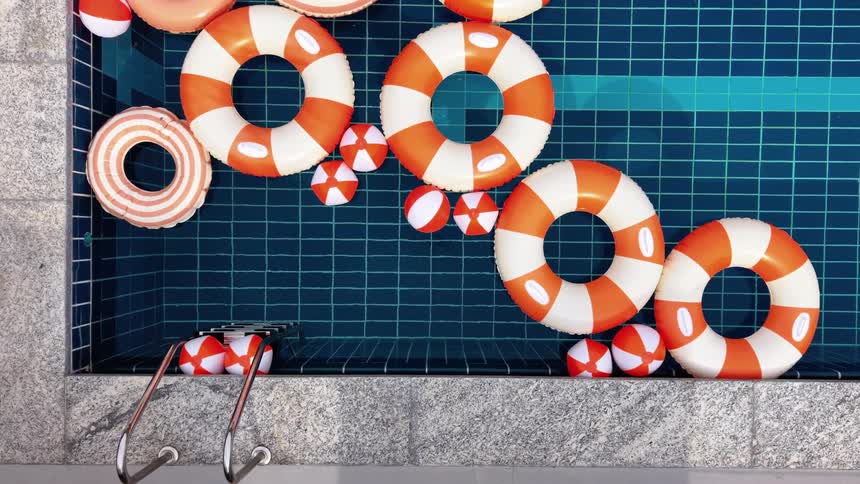 Empty swimming pool filled with orange and white inflatable rings and balls seen from above