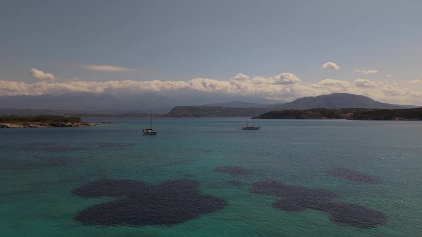 An aerial view from a luxury resort reveals a stunning turquoise bay with sailboats and distant mountains