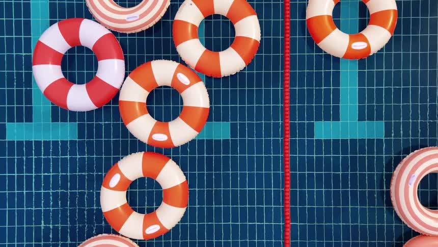 A top-down view of colorful red and white striped inflatable rings floating serenely in a blue tiled swimming pool