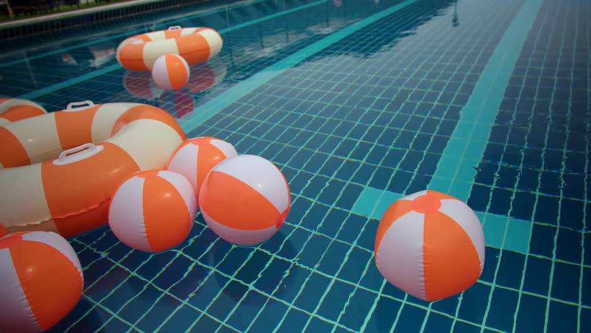 Orange and white striped inflatable beach balls and swim rings float gently in a blue tiled swimming pool