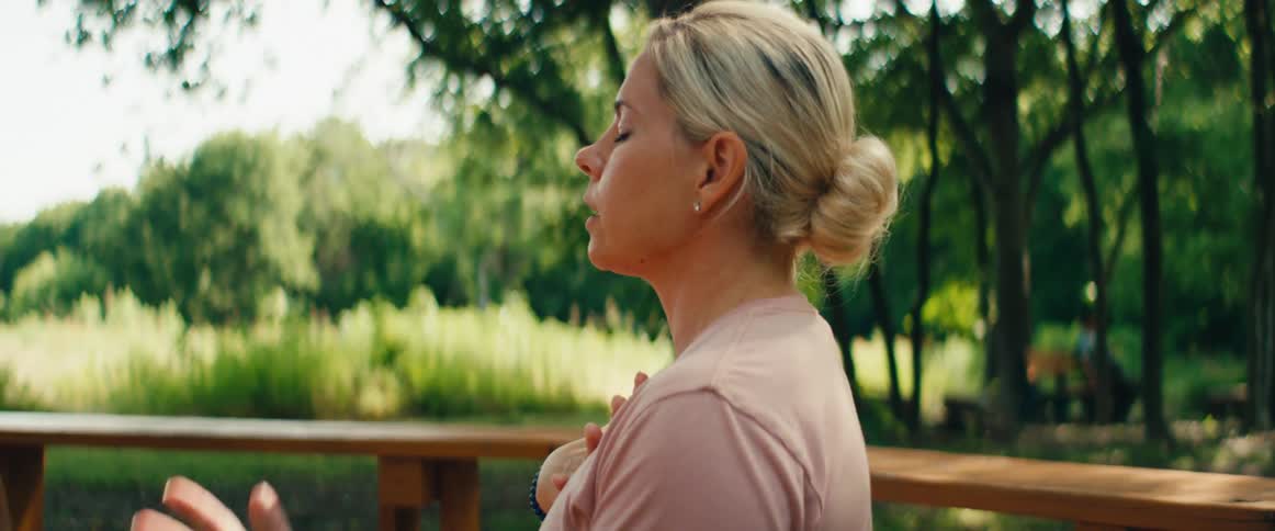 Close-up profile of a calm woman practicing mindfulness and deep breathing exercises in a lush green park