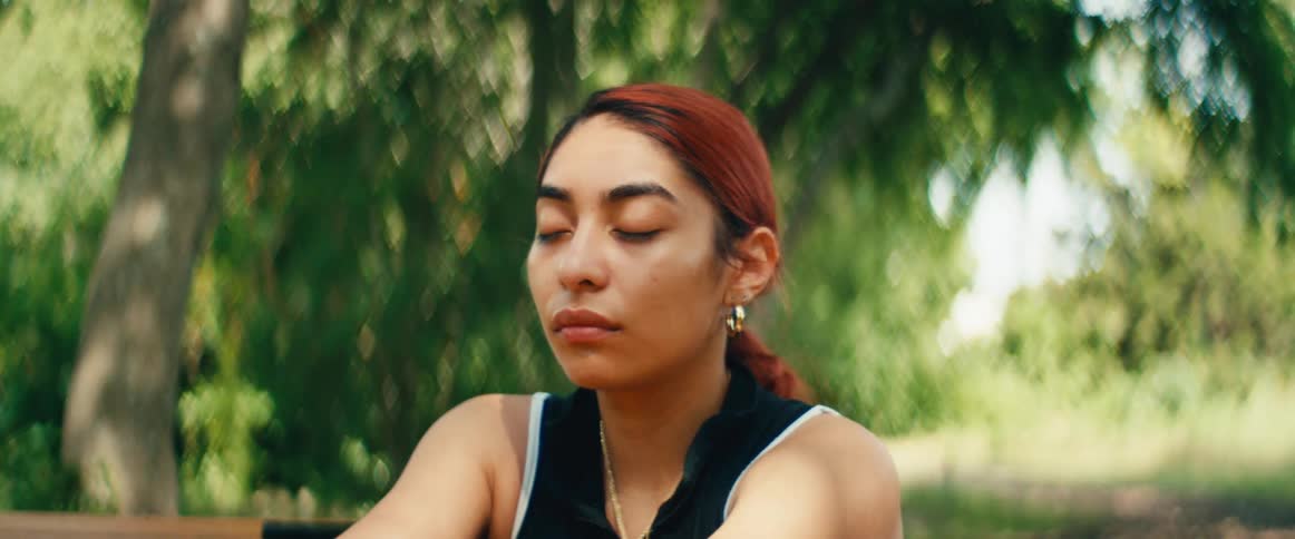 A serene young woman with red hair meditates peacefully outdoors in a lush green park