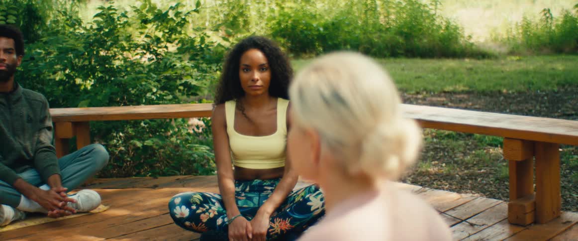 A focused young woman participates in a guided meditation session on a wooden deck in nature