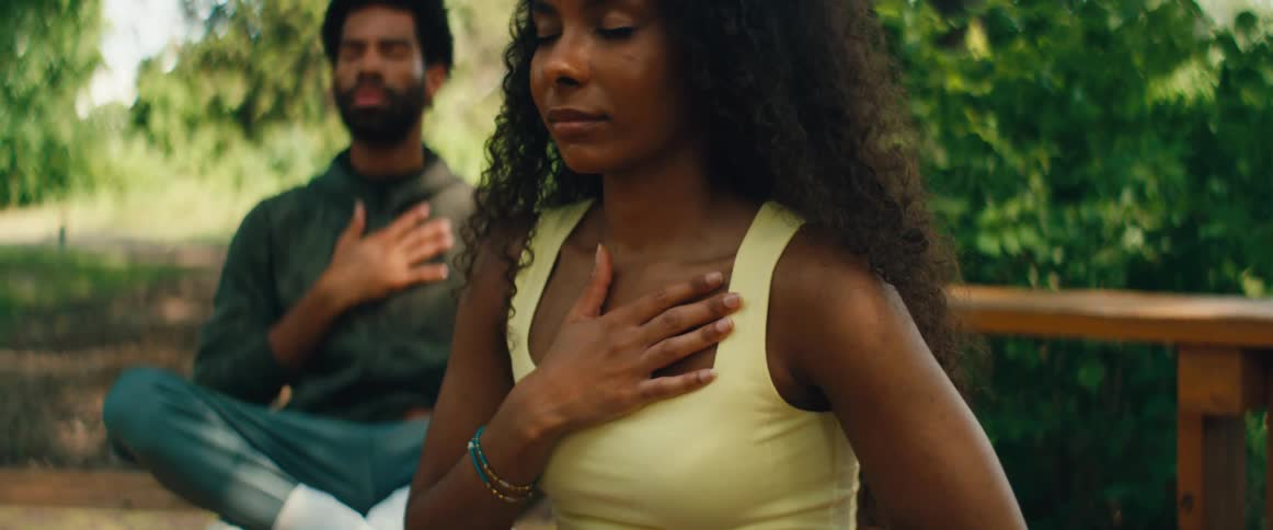 A serene couple practices mindfulness and meditation together with hands on their hearts in a lush green park