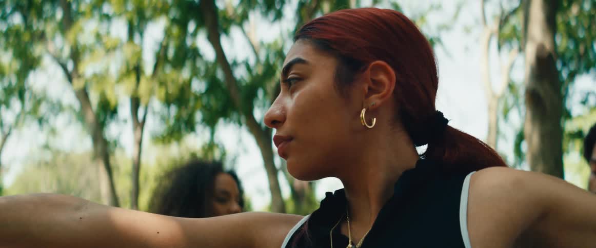 A close-up shot of a young woman with red hair holding a warrior II yoga pose with focus and determination in a park