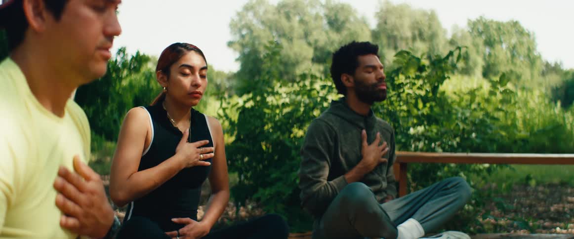 A diverse group of friends meditates with their eyes closed in a calm and peaceful outdoor park setting
