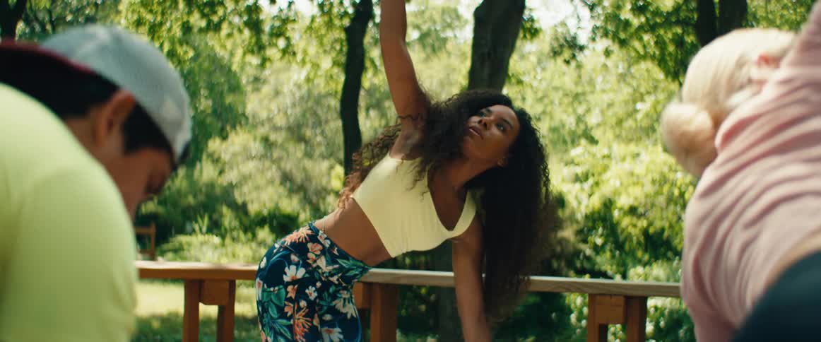 A beautiful, fit woman with long curly hair practices yoga stretches outdoors in slow motion on a wooden deck