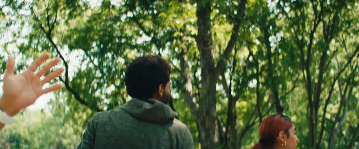 A slow-motion close-up of a man lowering his hand from the sky while standing next to a woman in a park