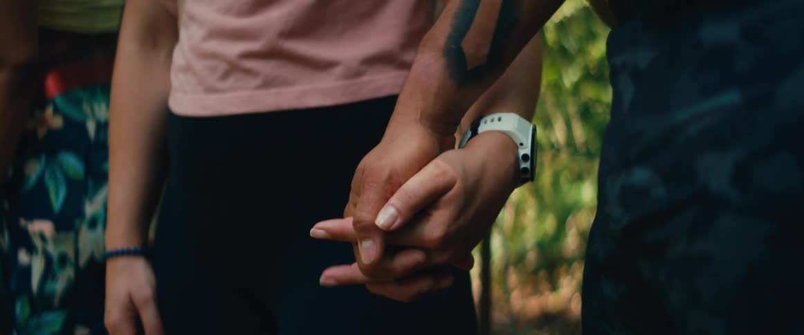 A slow-motion close-up of a couple gently reaching out and holding hands while standing in a lush, green forest