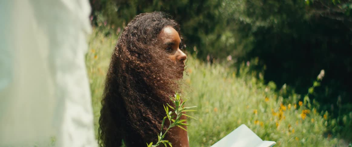 A peaceful woman with long curly hair enjoys a moment of reflection while reading in a sunlit wildflower field