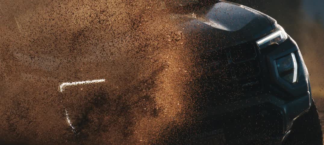 Close-up of a black GMC truck's front tire spinning and kicking up a massive cloud of mud and dirt in super slow motion