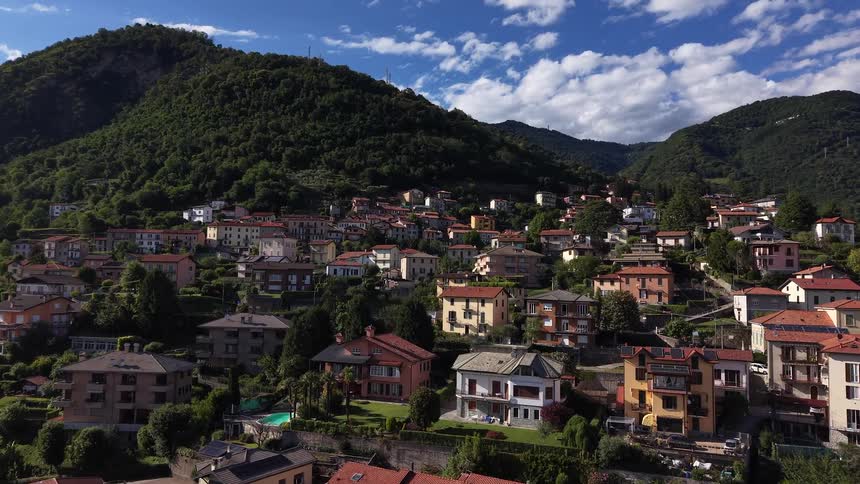 Scenic aerial footage slowly moves over a charming hillside town nestled in a green mountain valley in Italy