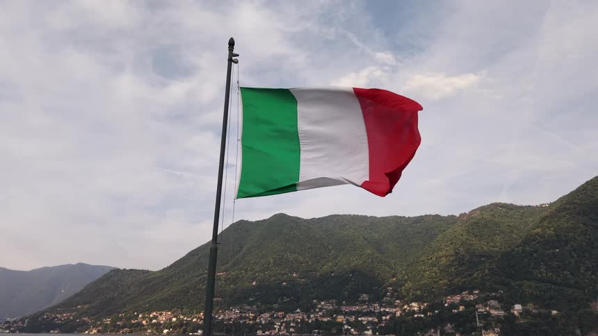 The Italian flag flutters proudly in slow motion against a picturesque backdrop of a lake and mountains