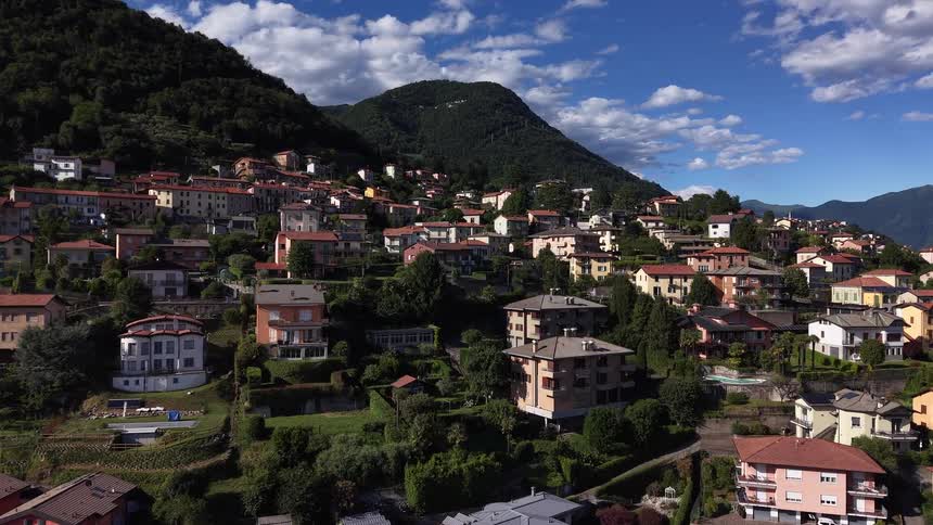 A beautiful aerial drone shot flying over a quaint town nestled in the green mountains of Lake Como, Italy on a sunny day