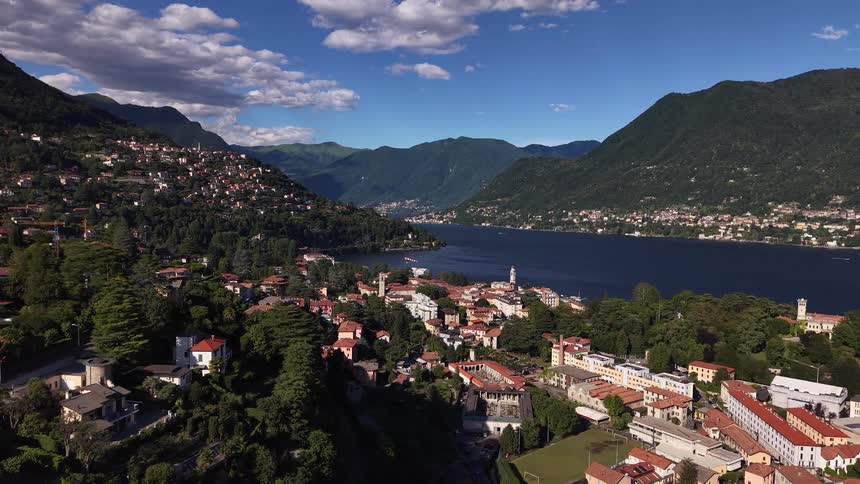 A slow aerial pullback reveals the stunning landscape of a town on Lake Como, Italy, nestled between towering green mountains