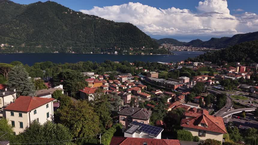 An aerial view flies forward over the town of Cernobbio on Lake Como in Italy, revealing a beautiful landscape of mountains, water, and classic architecture