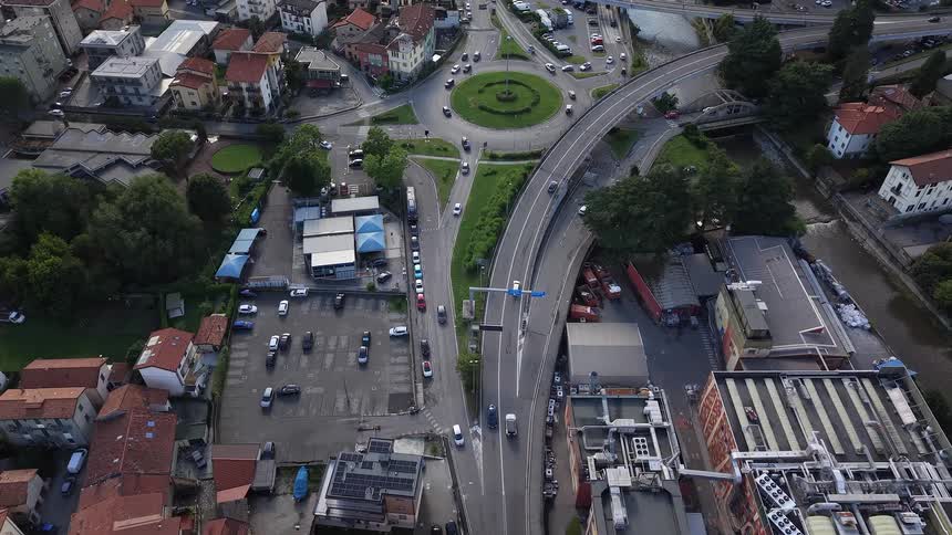 An aerial drone shot ascends over a bustling European roundabout with cars flowing through the city's road network
