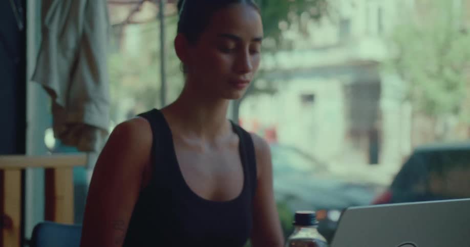 A young woman opens her laptop to begin working at a table by the window in a city cafe