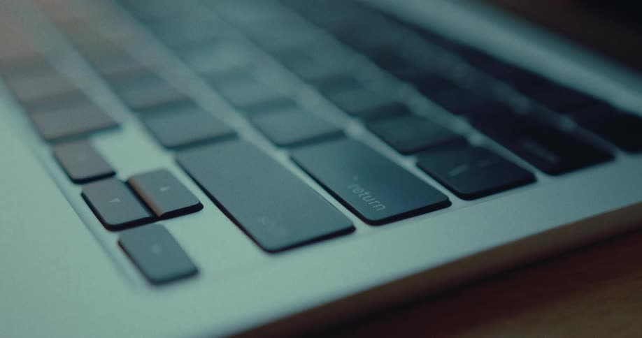 An extreme close-up shot shows a finger pressing the return key on a laptop keyboard in a dimly lit room
