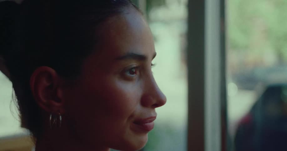 A close-up profile of a serene young woman taking a deep, calming breath while looking out a sunlit window