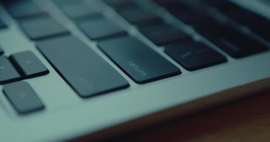 A close-up shot shows a finger pressing the return key on a laptop keyboard in a darkly lit room