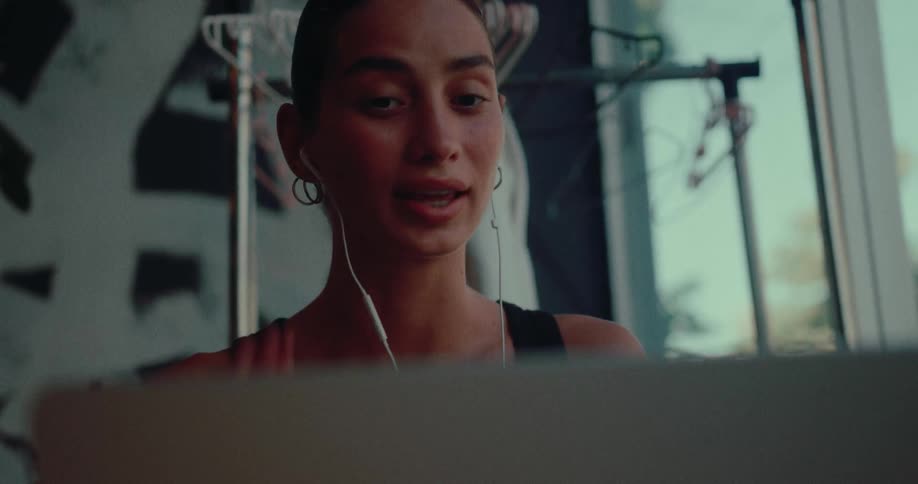 A young woman smiles and talks during a video conference call on her laptop while wearing earbuds