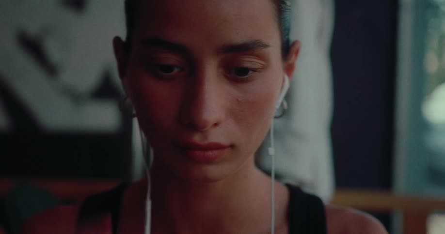 A close-up shot of a young woman with short hair putting in wired earbuds in a dimly lit room
