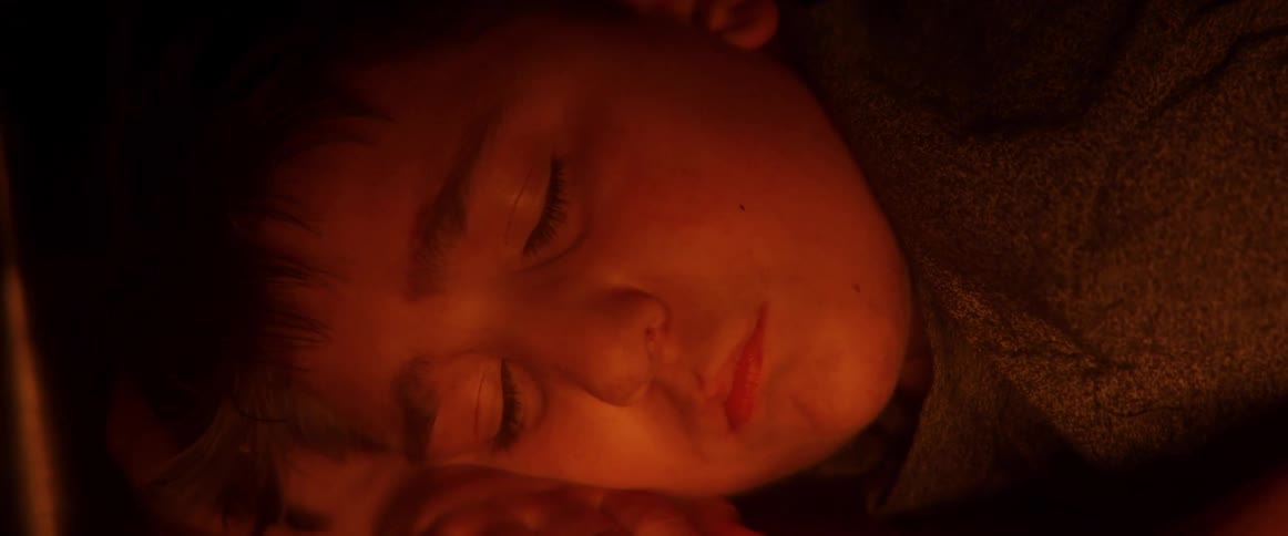 A sleepy young boy's face is illuminated by a warm, soft light as he slowly drifts off to sleep