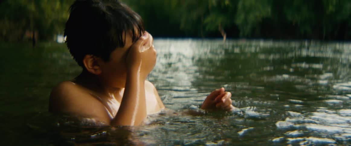 A joyful young boy finds serenity while swimming in a river, splashing happily before floating peacefully on his back