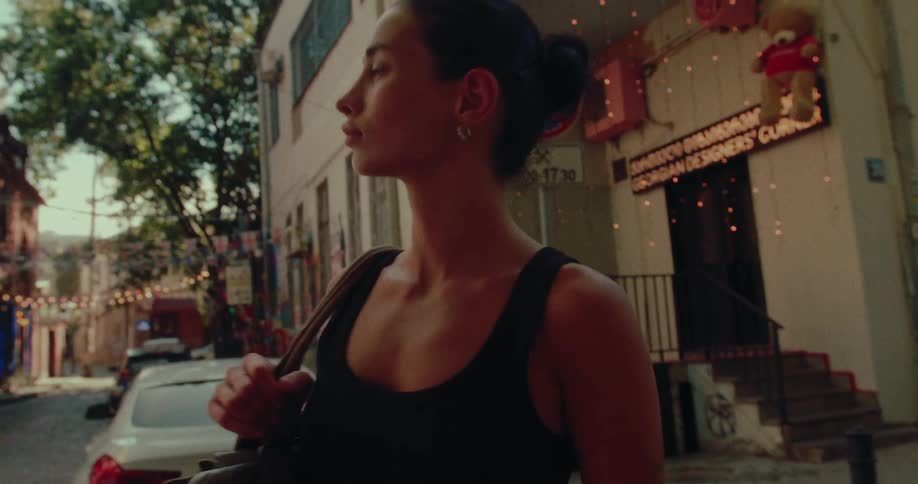 A stylish woman thoughtfully walks and pauses on a charming city street corner in beautiful slow motion