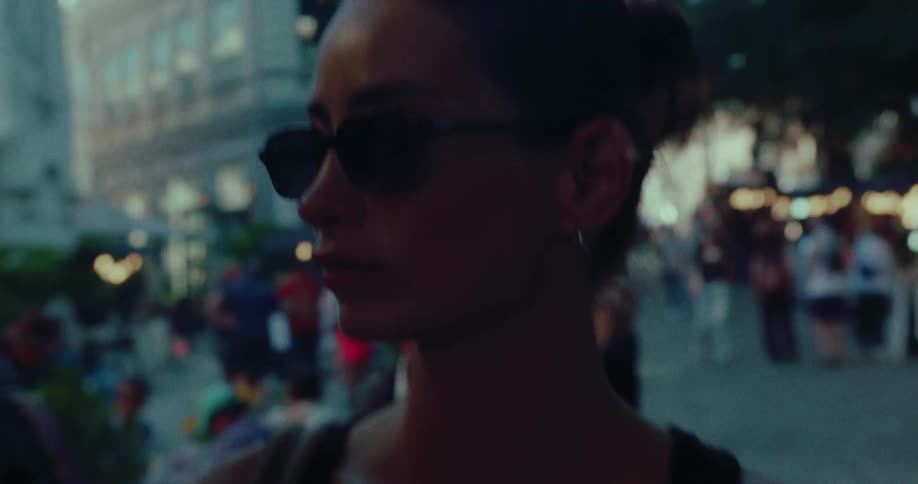 A beautiful young woman in sunglasses walks through a bustling city street market in the evening