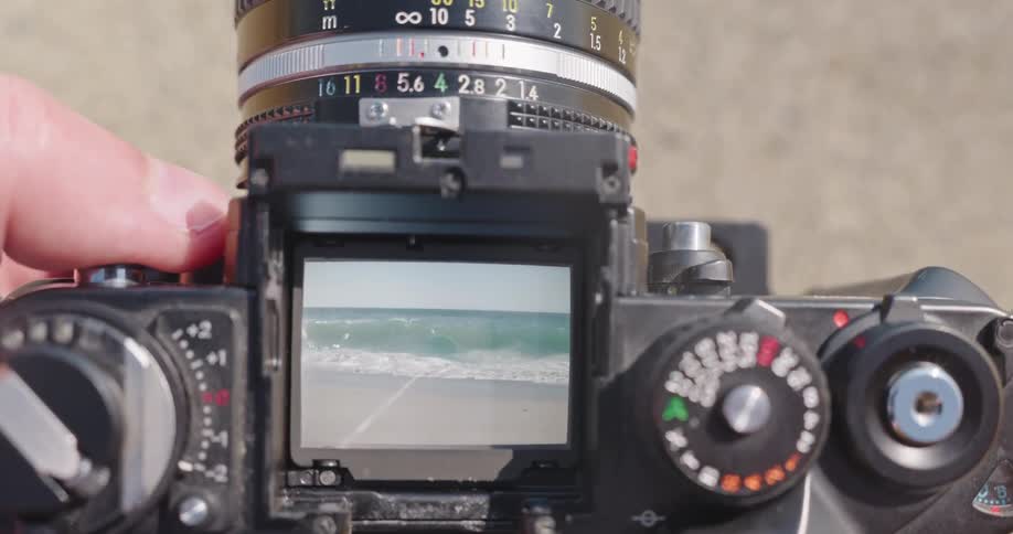 Looking through the viewfinder of an old film camera as ocean waves crash on the shore in slow motion