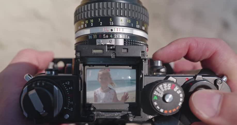 A photographer's point of view as they use a vintage film camera to take a picture of a smiling girl on a sunny beach