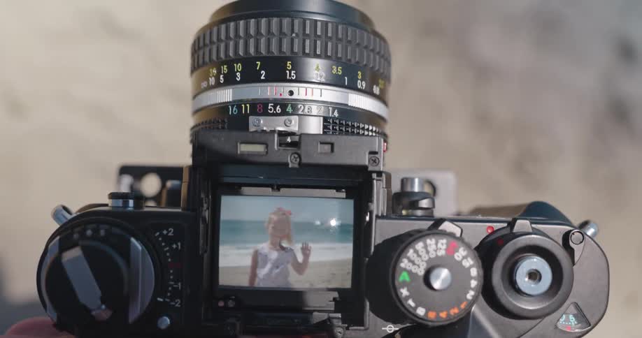 A photographer's point of view capturing a memory of a young girl waving on the beach through the viewfinder of a vintage film camera