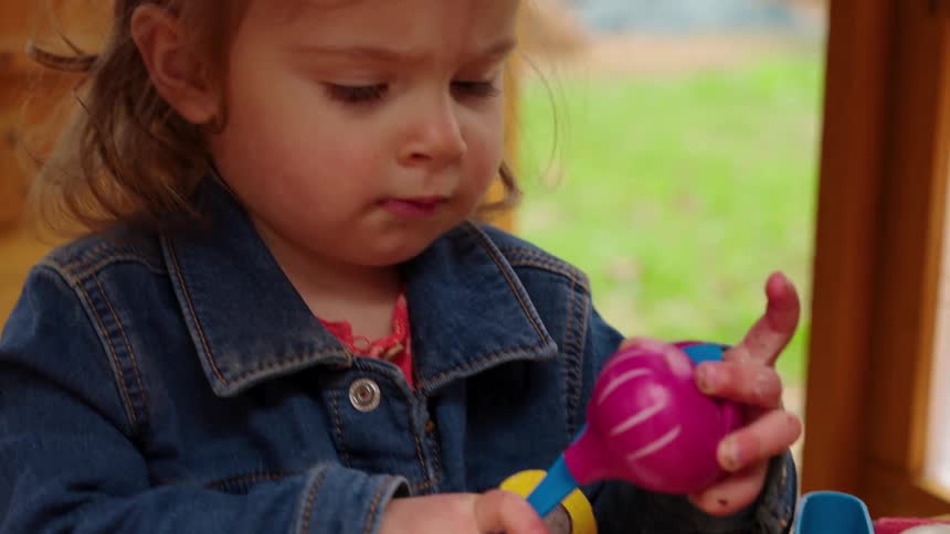 A cute toddler girl in a denim jacket intently plays with toy vegetables, cutting a purple onion in slow motion
